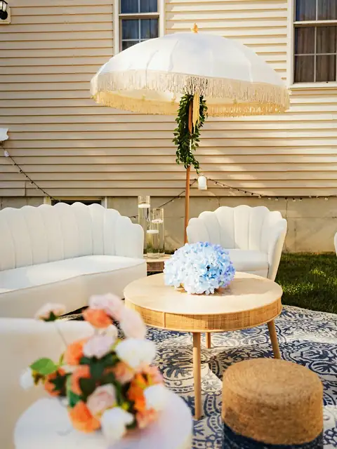 Backyard lounge with white scalloped sofas, a fringed umbrella and blue hydrangea arrangements