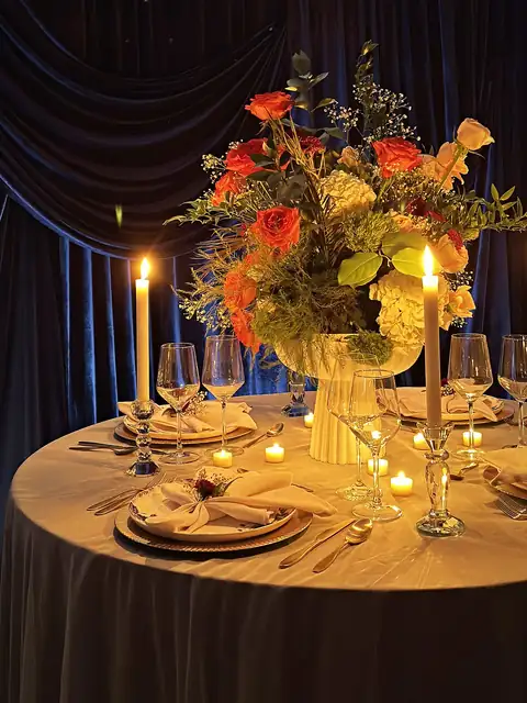 Candlelit round table with a coral rose and hydrangea centerpiece against navy velvet draping
