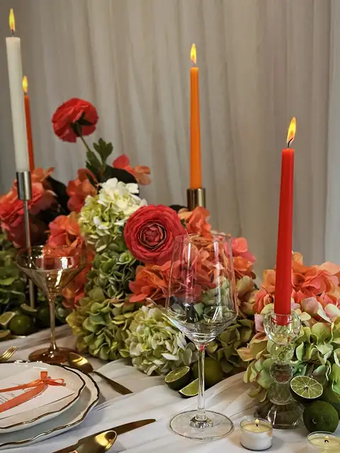 Coral, orange and ivory taper candles lit among coral ranunculus, sage hydrangea and limes on a head table