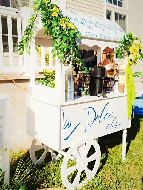 Custom chai cart dressed with yellow roses, greenery and a blue awning for a backyard celebration