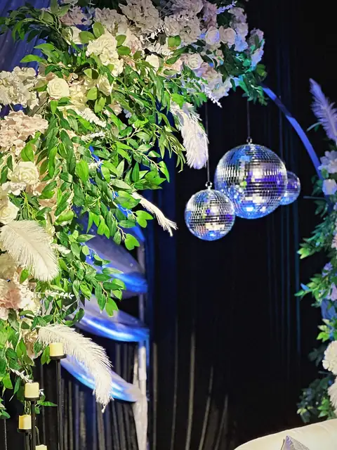 Mirror balls hanging inside a floral arch with white roses, blush hydrangea and ostrich feathers