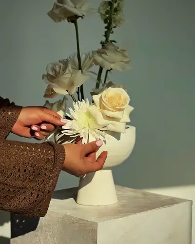 Mani arranging white roses and a chrysanthemum in a sculpted bowl in the Eden studio
