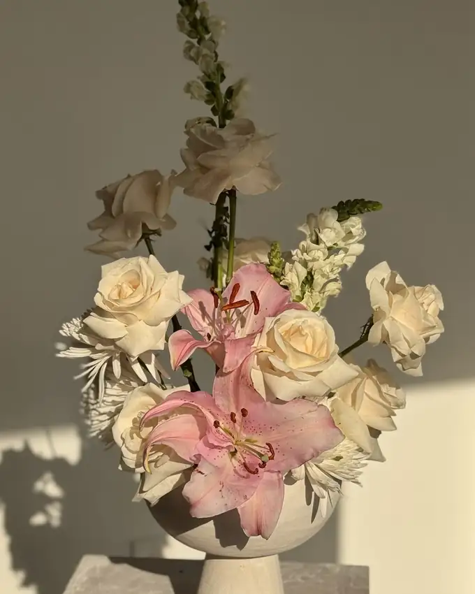 Fresh white garden roses, pink stargazer lilies and snapdragon in a white pedestal bowl, a bridal floral design by Eden Events & Co.
