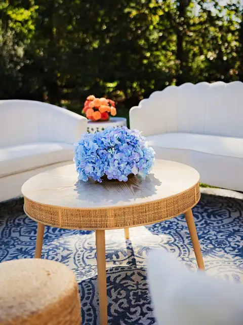 Blue hydrangea on a rattan table with coral roses and white scalloped sofas in a garden lounge