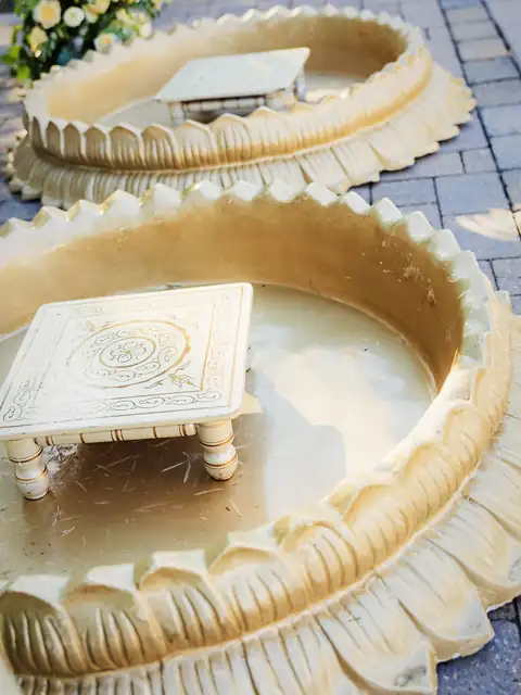 Gold lotus-shaped haldi tubs with hand-painted chowki stools on a stone patio