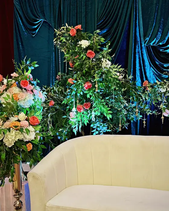 Ivory loveseat before emerald velvet draping, framed by tall floral arrangements of peach roses and ivory blooms