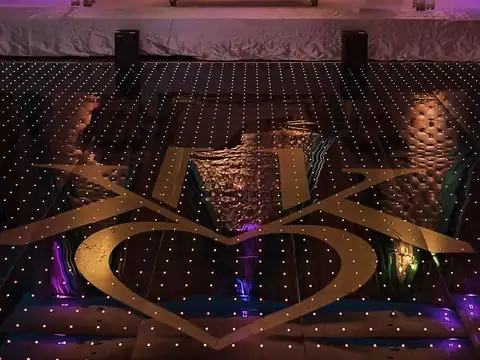 Lit LED dance floor with a gold custom monogram in front of a tufted blush stage and gold chaise
