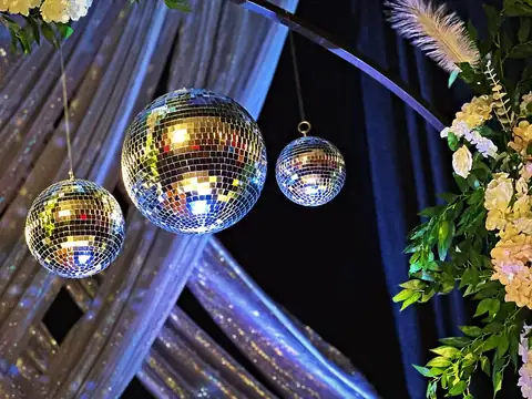 Three mirror balls hanging from a floral arch with feathers and silver sequin drapes