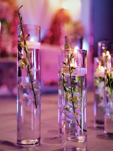 Orchid stems suspended in glass cylinders with floating candles and a pink stage glow behind