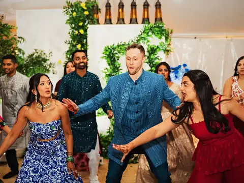 Groom and guests dancing a choreographed sangeet number in front of a greenery monogram stage