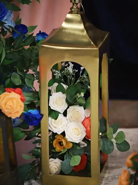 Gold lantern filled with ivory roses beside coral and blue florals against peach drapes