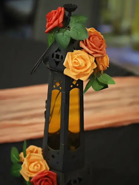 Black lantern with amber glass wrapped in coral and orange roses over a peach runner