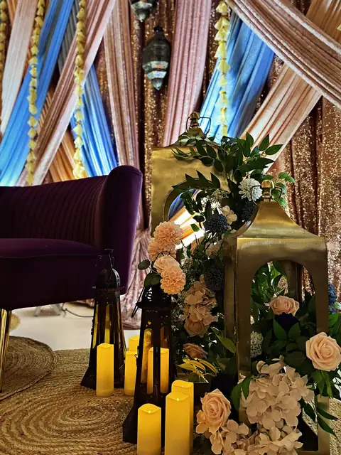 Pastel drapes with gold lanterns, pillar candles and blush florals beside a plum velvet loveseat