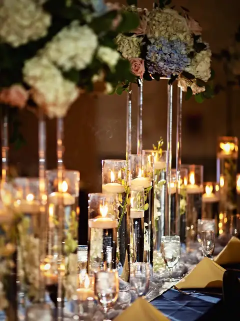 Tall hydrangea and rose centerpieces above floating candles in glass cylinders on a navy reception head table