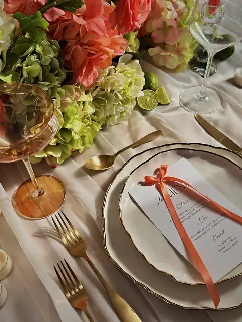 Wedding place setting with a gold-rimmed plate, a menu tied in coral ribbon, gold flatware, sage hydrangeas and limes