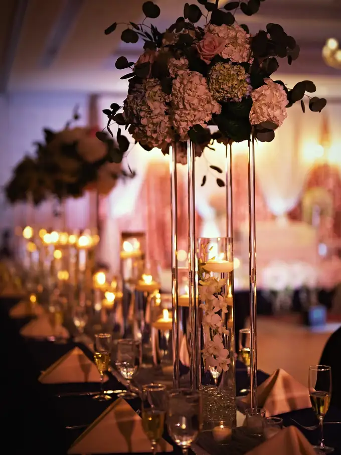 Tall hydrangea and rose centerpiece with floating candles glowing down a wedding reception table, designed by Eden Events & Co.