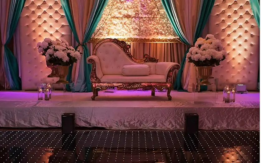 Gold baroque chaise on a tufted blush stage with teal drapes and a lit LED dance floor in front
